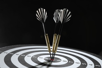 Photo of Targeting. Dart board with arrows on black background, closeup