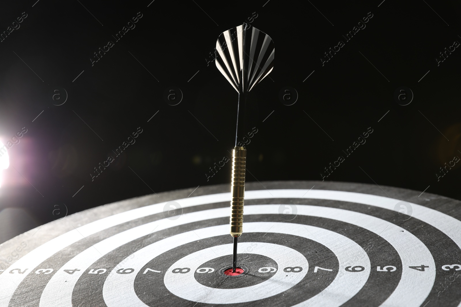 Targeting. Dart board with arrow on dark background, closeup Photo of Targeting. Dart board with arrow on dark background, closeup