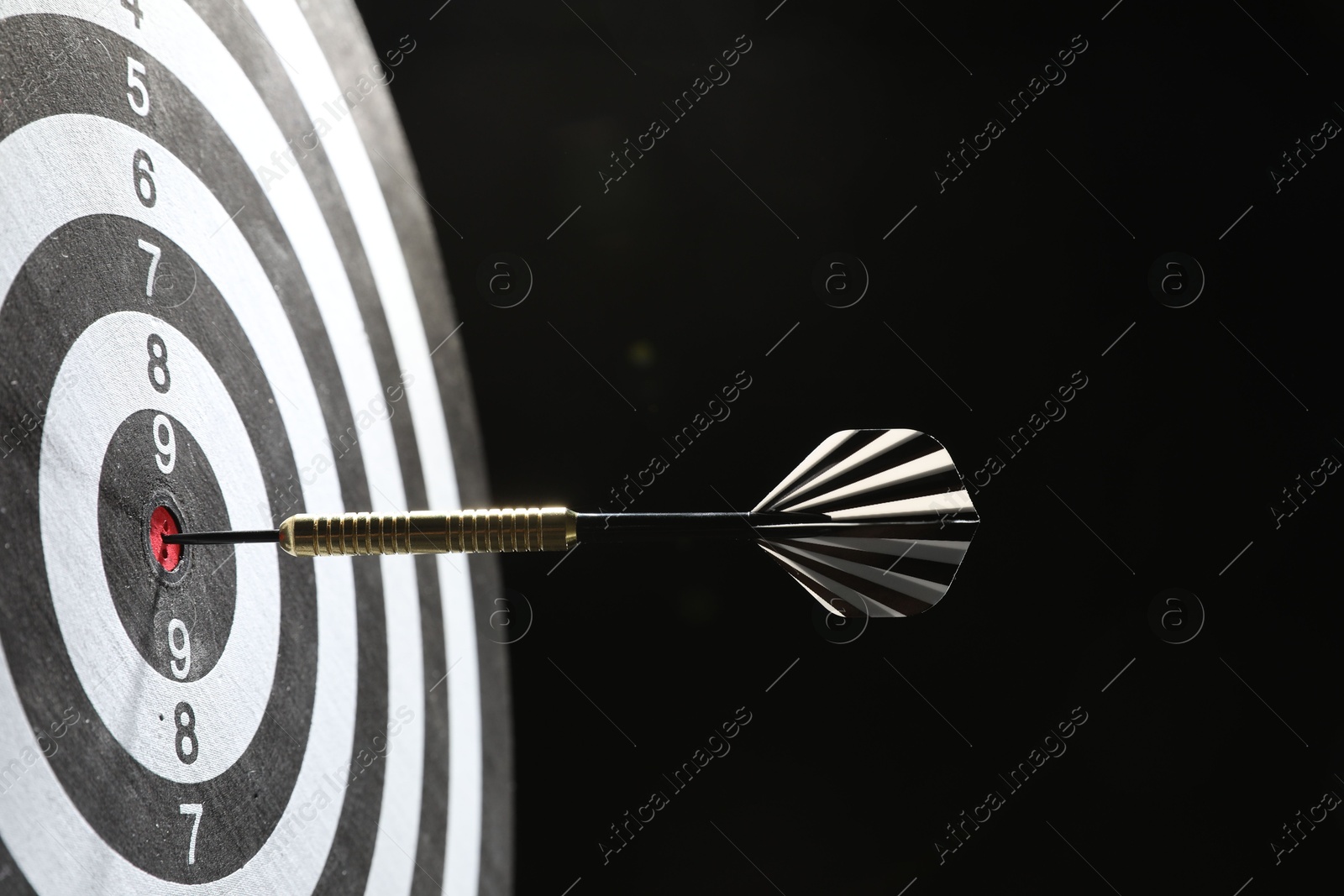 Targeting. Dart board with arrow on dark background, closeup Photo of Targeting. Dart board with arrow on dark background, closeup