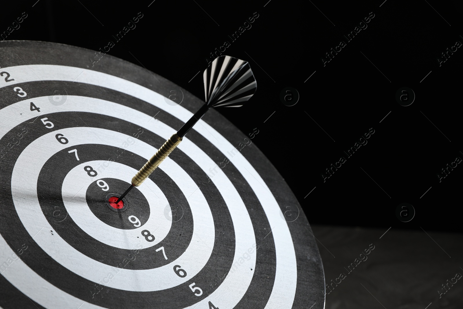 Targeting. Dart board with arrow on dark background, closeup Photo of Targeting. Dart board with arrow on dark background, closeup