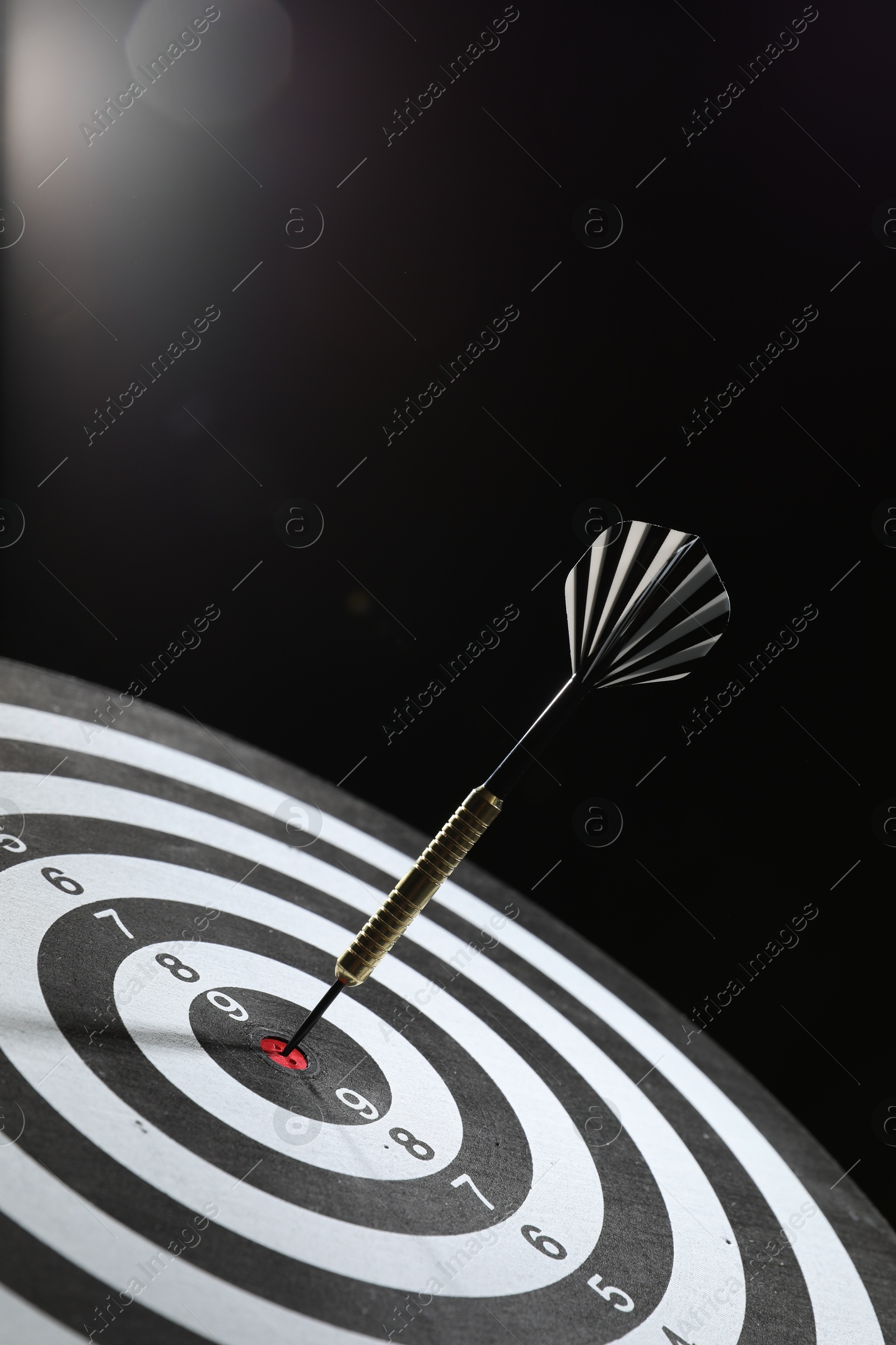 Targeting. Dart board with arrow on dark background, closeup Photo of Targeting. Dart board with arrow on dark background, closeup