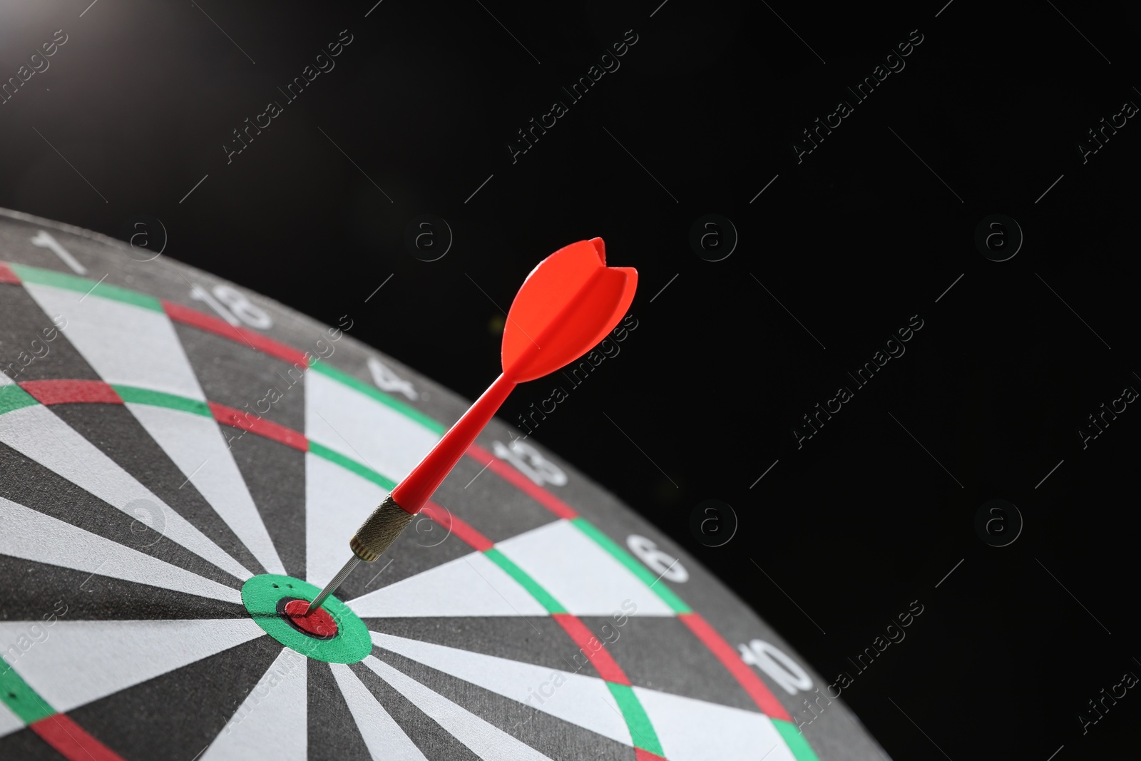 Targeting. Dart board with arrow on dark background, closeup Photo of Targeting. Dart board with arrow on dark background, closeup