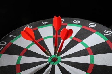 Photo of Targeting. Dart board with arrows on black background, closeup