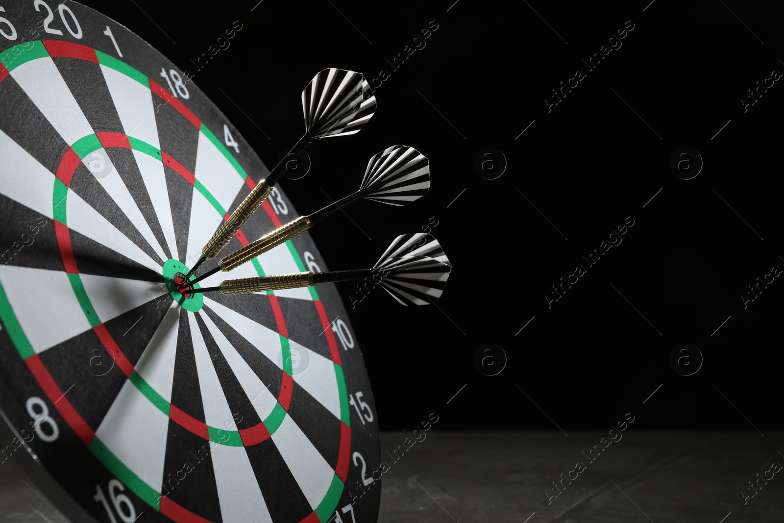 Targeting. Dart board with arrows on dark background, closeup. Space for text Photo of Targeting. Dart board with arrows on dark background, closeup. Space for text