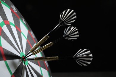 Photo of Targeting. Dart board with arrows on black background, closeup