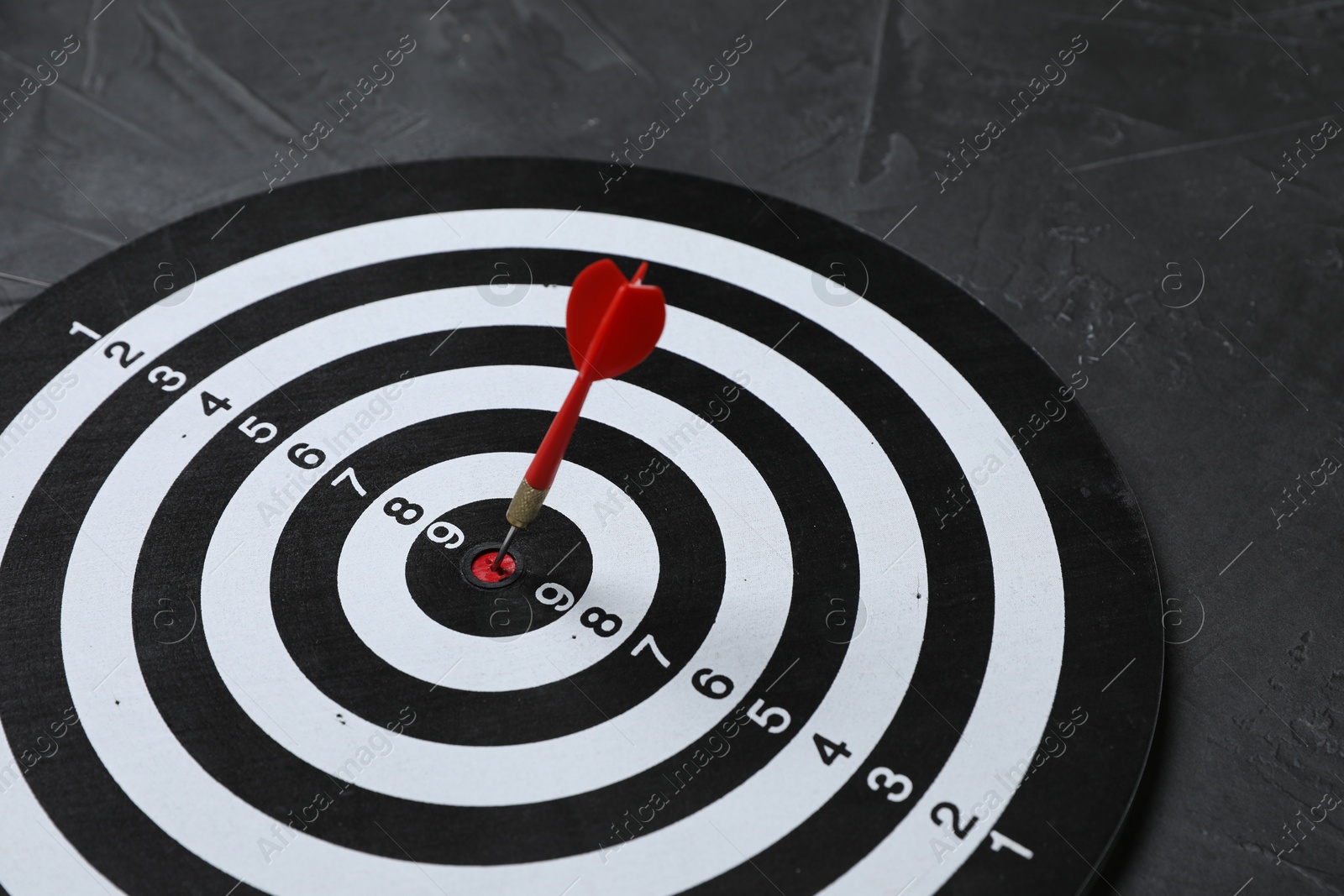Targeting. Dart board with arrow on gray background, closeup Photo of Targeting. Dart board with arrow on gray background, closeup