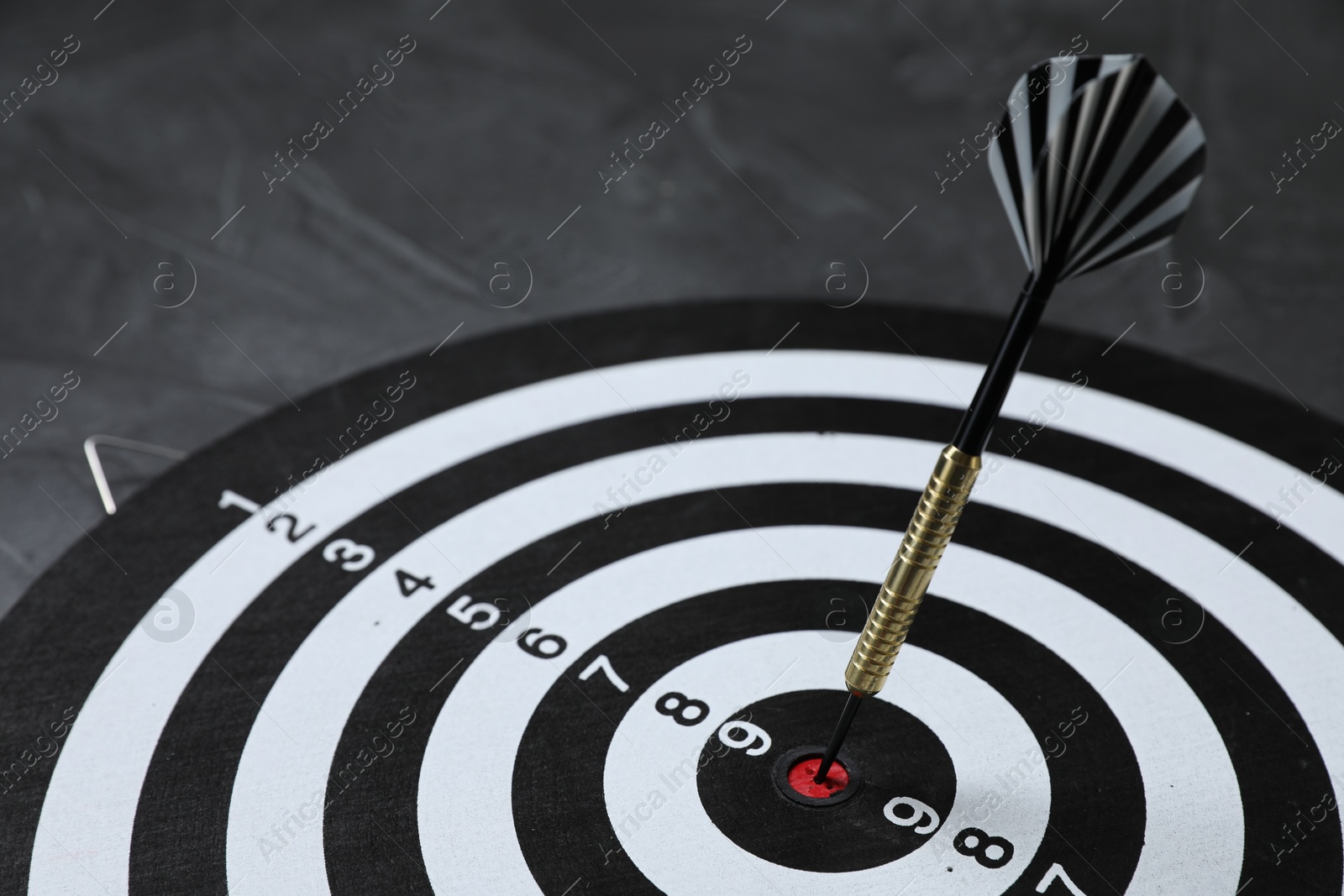 Targeting. Dart board with arrow on gray background, closeup Photo of Targeting. Dart board with arrow on gray background, closeup