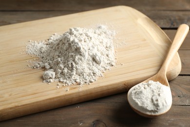 Photo of Pile of flour and spoon on wooden table, closeup