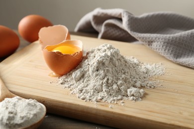 Photo of Pile of flour and broken egg on wooden table against grey background, closeup