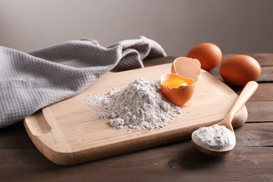Photo of Pile of flour, spoon and broken egg on wooden table against grey background, closeup