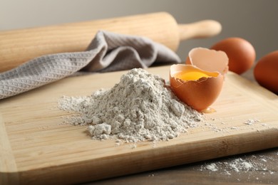 Photo of Pile of flour and broken egg on wooden table against grey background, closeup