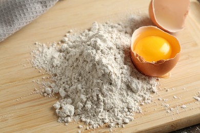 Photo of Pile of flour and broken egg on wooden board, closeup