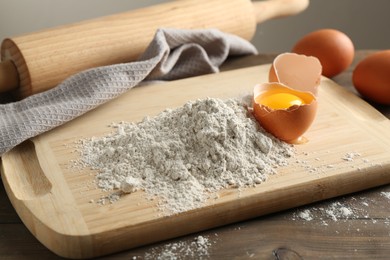 Photo of Pile of flour and broken egg on wooden table against grey background, closeup