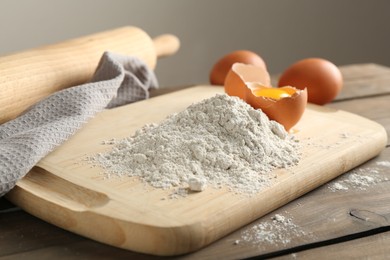 Photo of Pile of flour and broken egg on wooden table against grey background, closeup