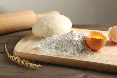 Photo of Pile of flour, broken egg and dough on wooden table against grey background, closeup