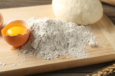 Photo of Pile of flour, broken egg and dough on wooden table, closeup