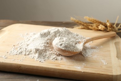 Photo of Pile of flour and spoon on wooden table against grey background, closeup