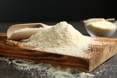 Photo of Pile of flour and scoop on dark wooden table against black background, closeup