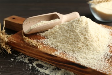 Photo of Pile of flour, spikes and scoop on dark wooden table, closeup