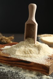 Photo of Pile of flour and scoop on dark table against black background, closeup