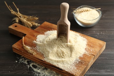 Photo of Pile of flour, spikes and scoop on dark wooden table, closeup