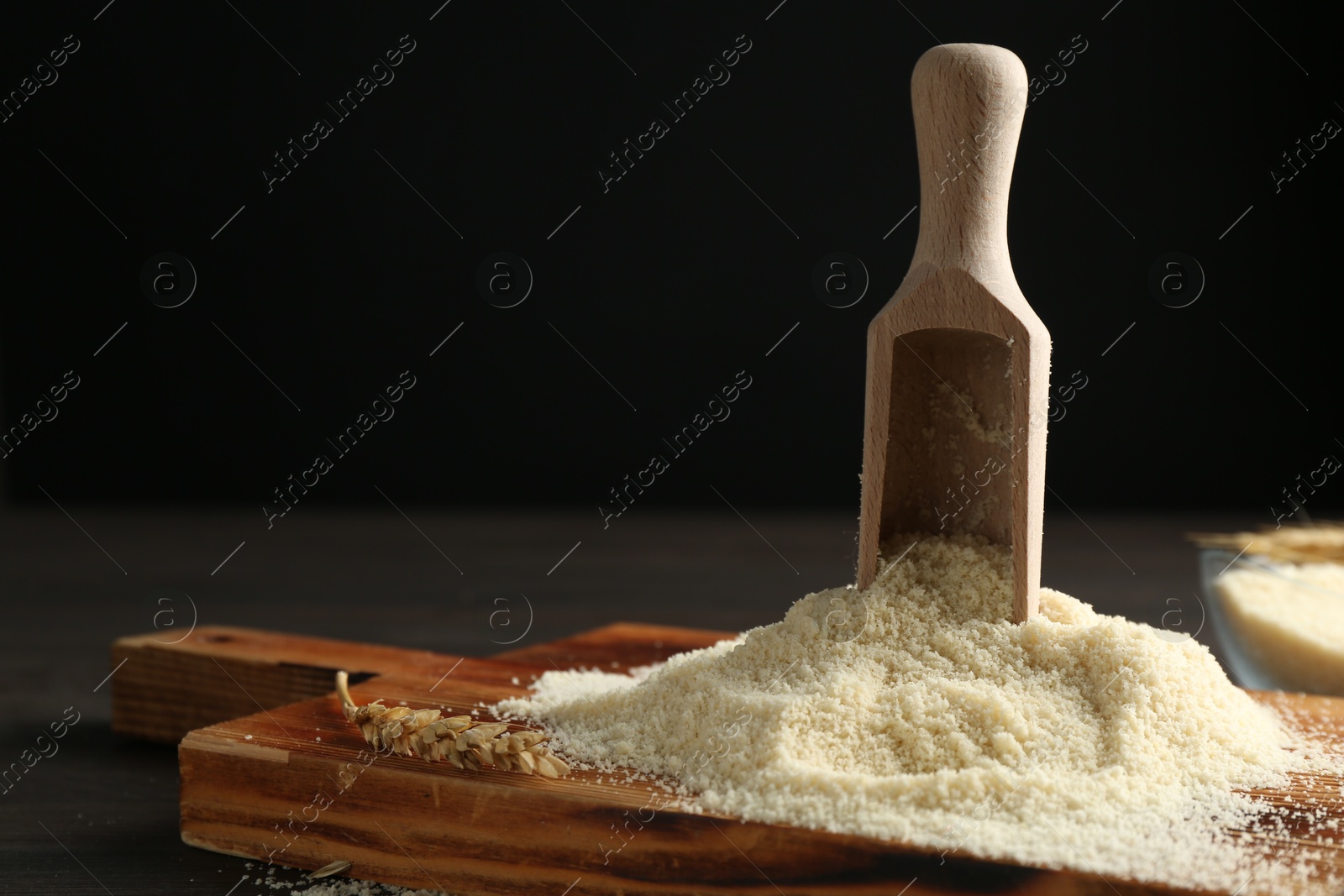Photo of Pile of flour and scoop on dark wooden table against black background, closeup