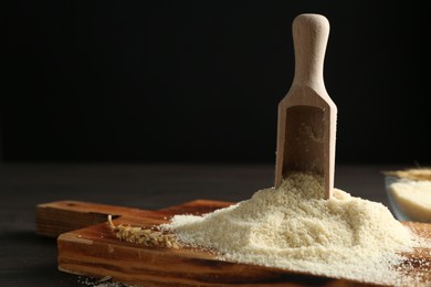Photo of Pile of flour and scoop on dark wooden table against black background, closeup