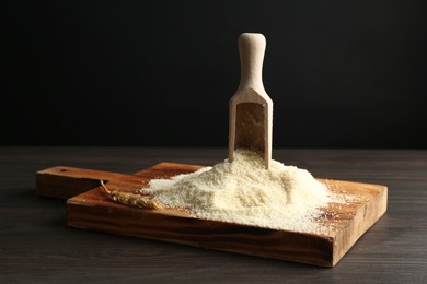 Photo of Pile of flour and scoop on dark wooden table against black background, closeup