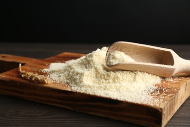 Photo of Pile of flour and scoop on dark wooden table against black background, closeup