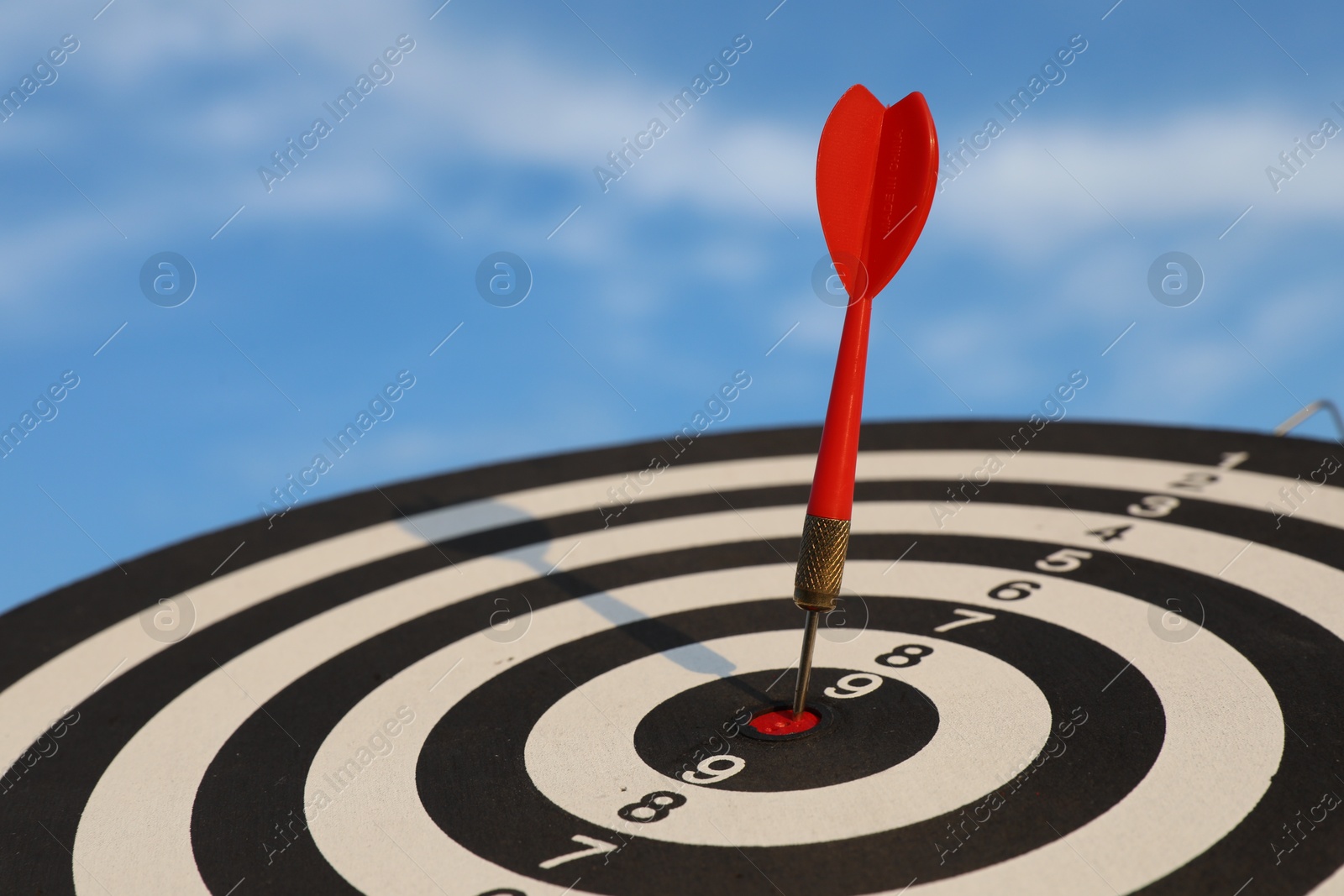 Targeting. Dart board with arrow against blue sky, closeup Photo of Targeting. Dart board with arrow against blue sky, closeup