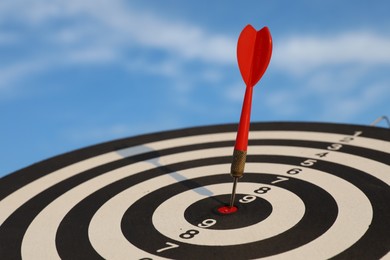 Photo of Targeting. Dart board with arrow against blue sky, closeup