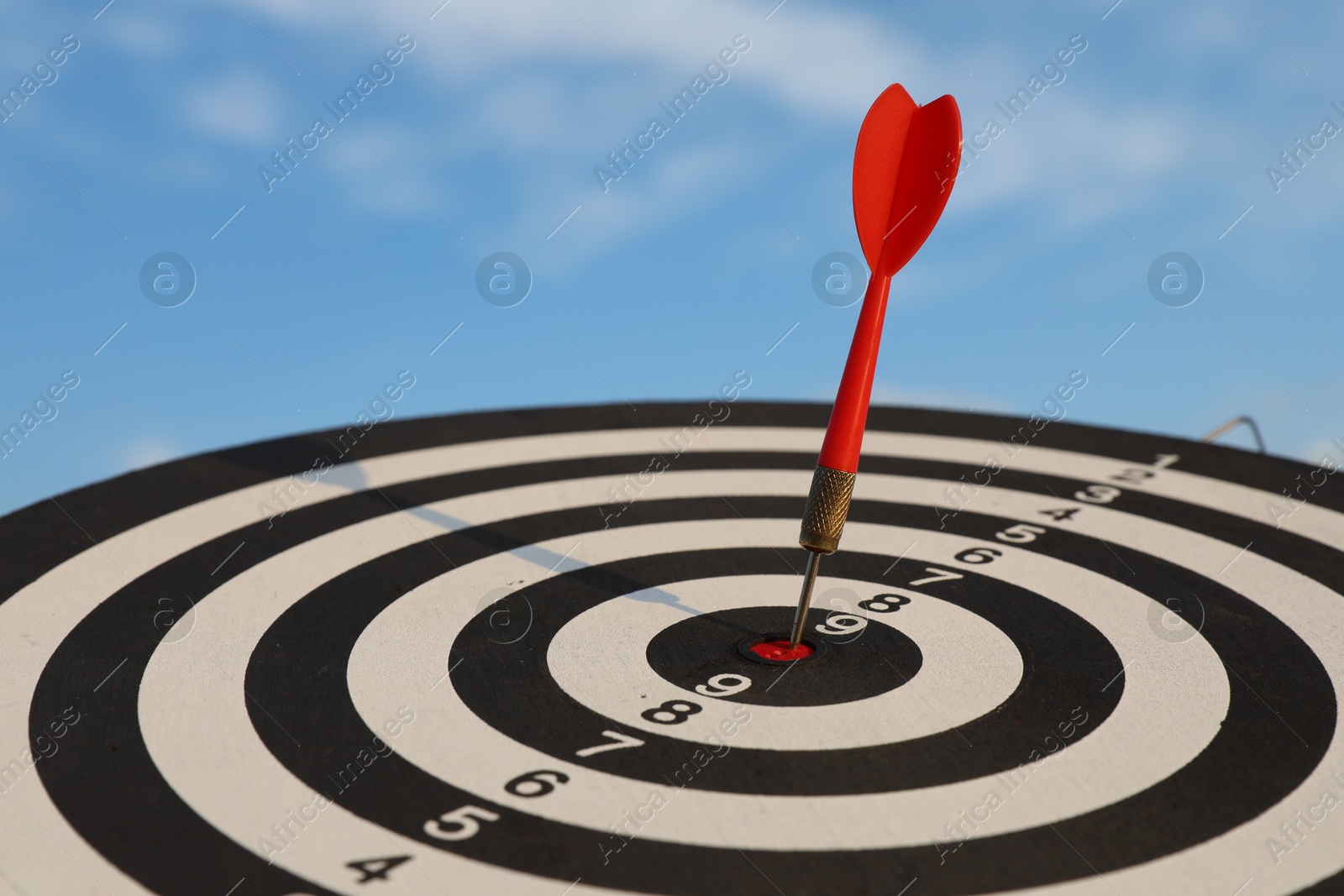 Targeting. Dart board with arrow against blue sky, closeup Photo of Targeting. Dart board with arrow against blue sky, closeup