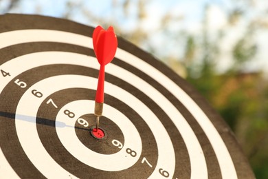 Photo of Targeting. Dart board with arrow outdoors, closeup