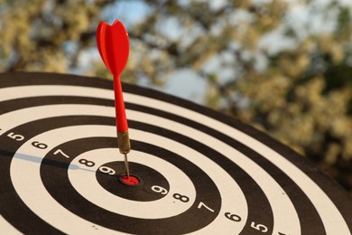 Photo of Targeting. Dart board with arrow outdoors, closeup
