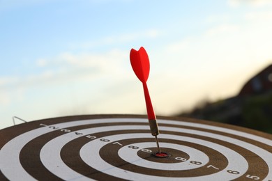 Photo of Targeting. Dart board with arrow outdoors, closeup