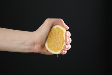 Photo of Woman squeezing lemon on black background, closeup