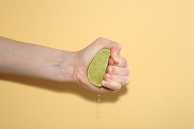 Photo of Woman squeezing lime on yellow background, closeup