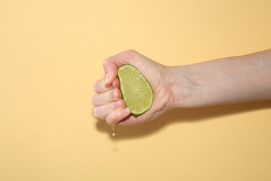 Photo of Woman squeezing lime on yellow background, closeup