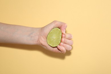 Photo of Woman squeezing lime on yellow background, closeup