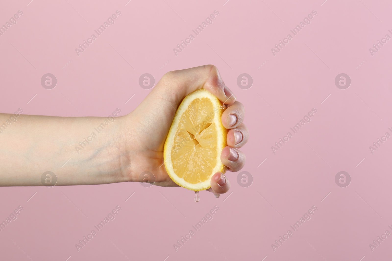 Woman squeezing lemon on pink background, closeup Photo of Woman squeezing lemon on pink background, closeup