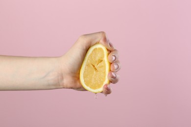 Photo of Woman squeezing lemon on pink background, closeup