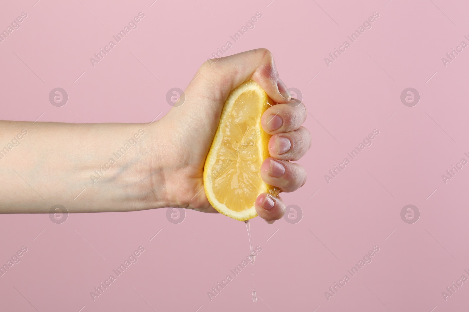 Woman squeezing lemon on pink background, closeup Photo of Woman squeezing lemon on pink background, closeup