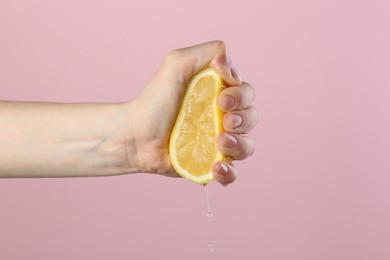 Photo of Woman squeezing lemon on pink background, closeup