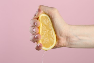 Photo of Woman squeezing lemon on pink background, closeup