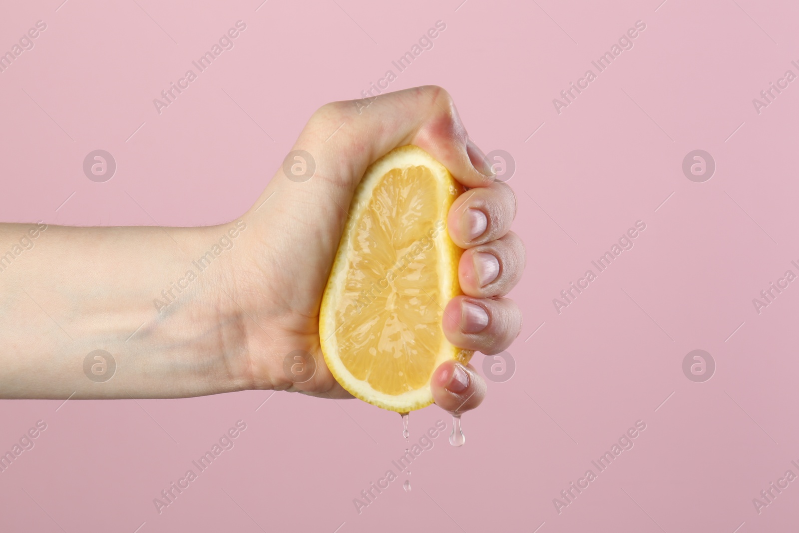 Woman squeezing lemon on pink background, closeup Photo of Woman squeezing lemon on pink background, closeup