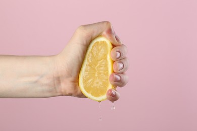Photo of Woman squeezing lemon on pink background, closeup