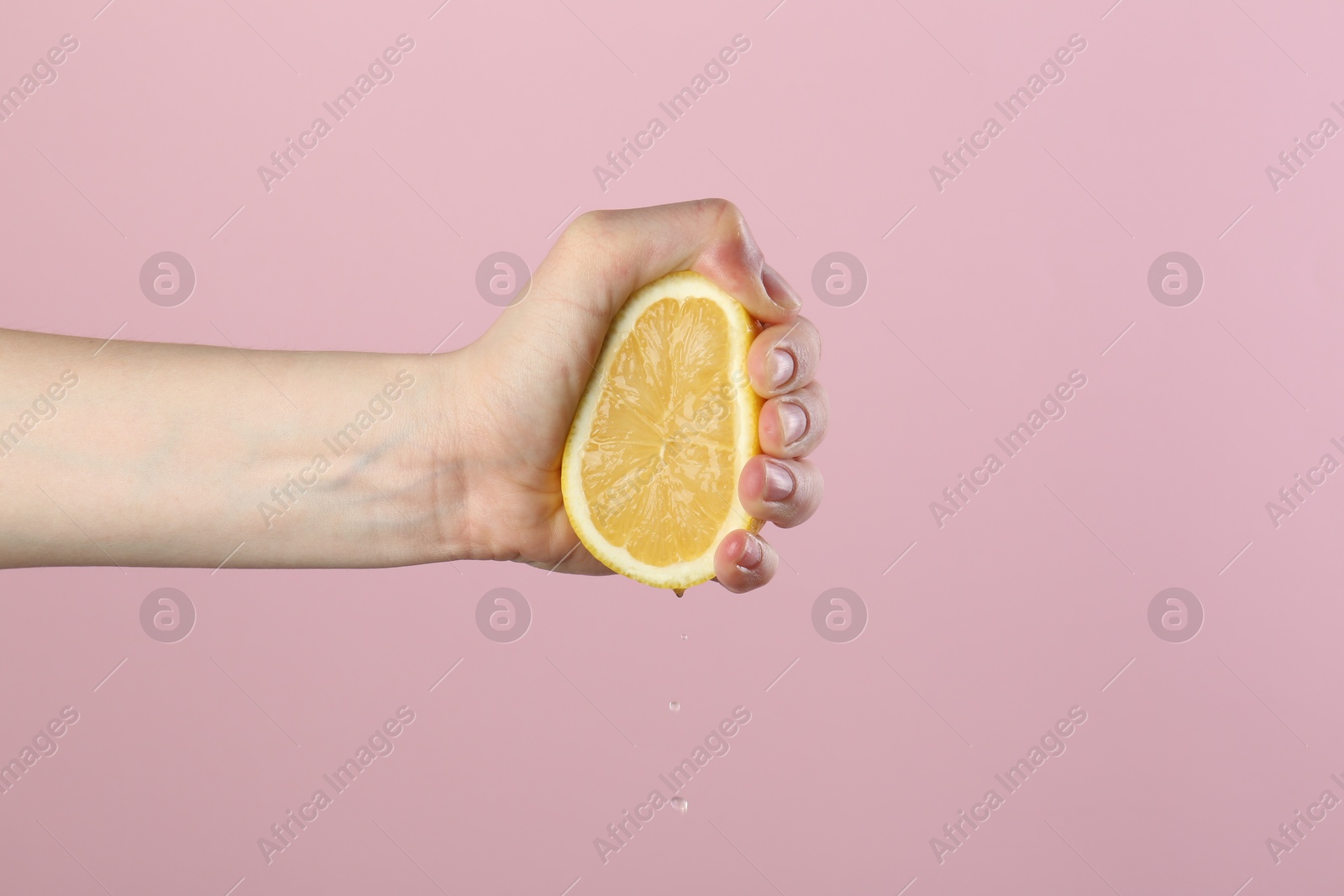 Woman squeezing lemon on pink background, closeup Photo of Woman squeezing lemon on pink background, closeup