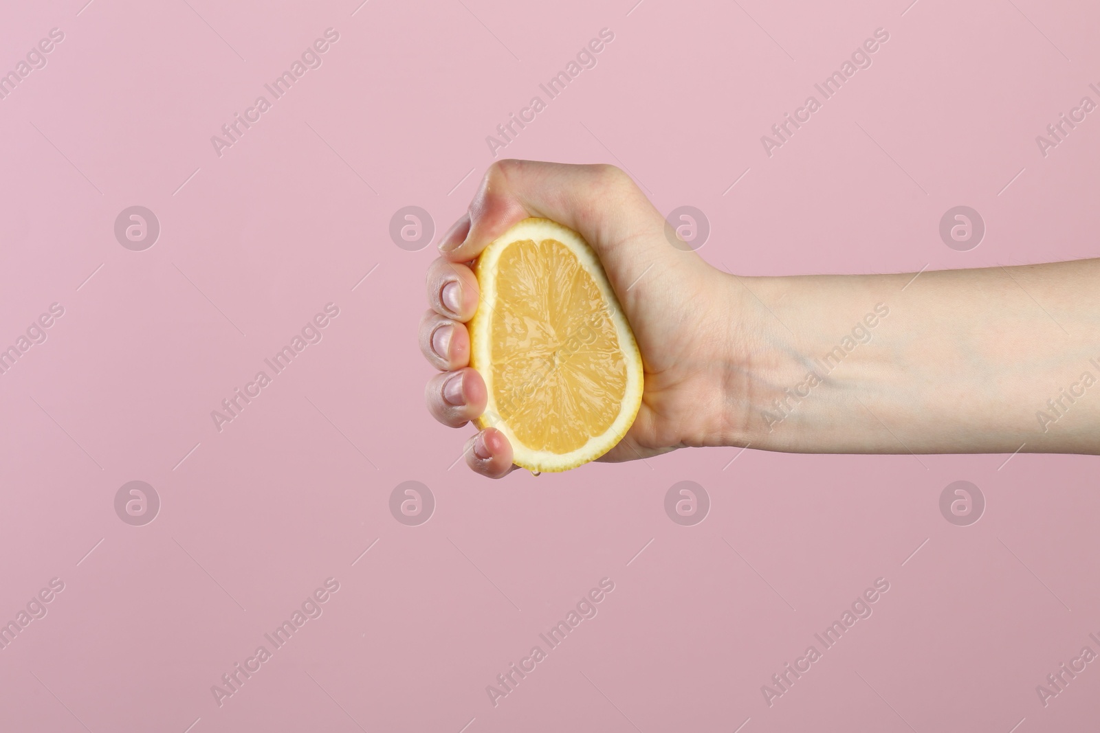 Woman squeezing lemon on pink background, closeup Photo of Woman squeezing lemon on pink background, closeup