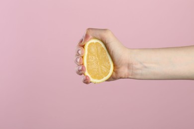 Photo of Woman squeezing lemon on pink background, closeup