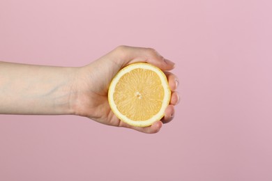 Photo of Woman squeezing lemon on pink background, closeup